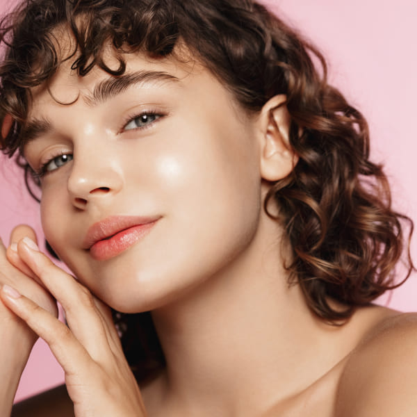 Une femme aux cheveux bouclés sur un fond rose.