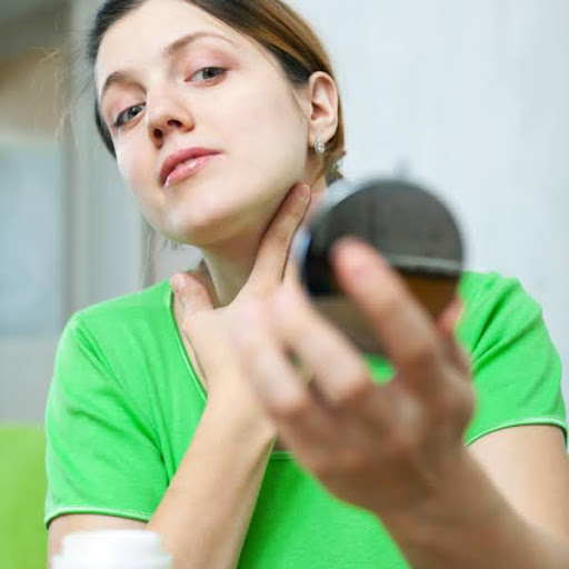 Femme appliquant un soin topique sur ses cicatrices d'acné en se regardant dans un petit miroir