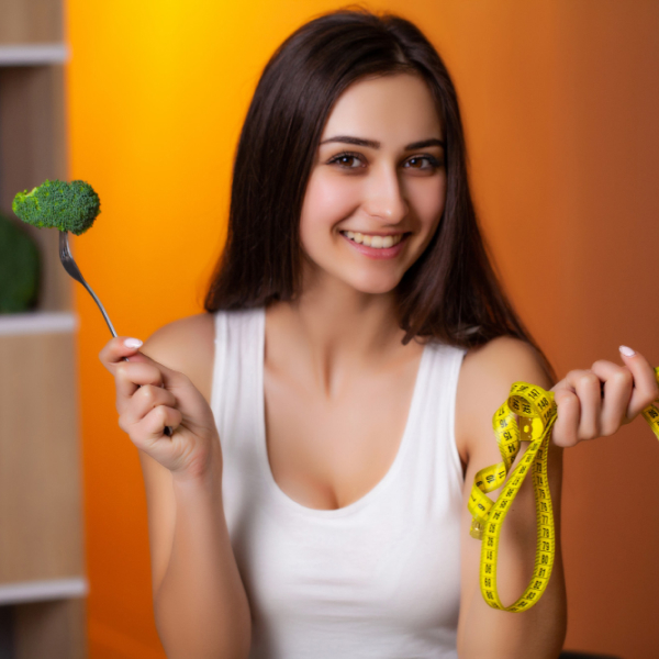 Femme souriante tenant une fourchette avec du brocoli et un ruban à mesurer, symbolisant une perte de poids saine